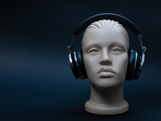dummy mannequin head with over ear headphones on black background, low key image