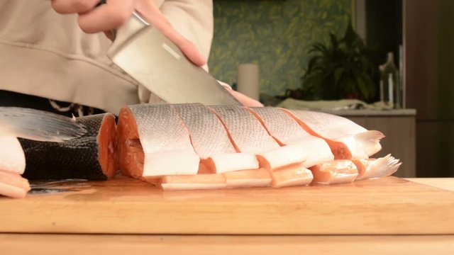Close-up of female hands are cutting with a knife a large salmon on a wooden table of home cooking