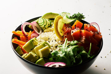 poke bowl with salmon, avocado, cucumber, arugula, broccoli, rice, carrot and sweet onions isolated over white background. side view
