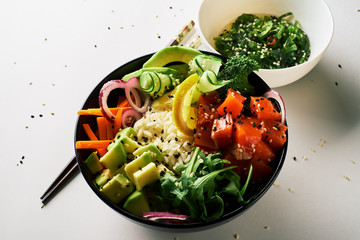 poke bowl with salmon, avocado, cucumber, arugula, broccoli, rice, carrot and sweet onions with chuka salad, chopsticks isolated over white background. top view