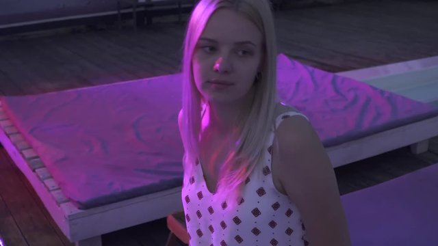 Beautiful girl drinks a cocktail while sitting at the bar on the summer terrace. Cute lonely blonde drinking cocktail in a nightclub.