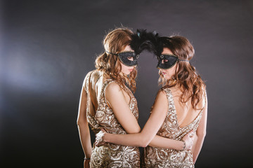 Portrait of two women dancers in max-size masks and gold dresses