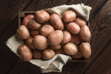 a pile of fresh potatoes in a dark wooden box. Linen canvas background.