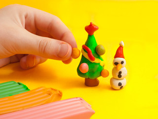Christmas children's craft of plasticine. A green Christmas tree with balls, toys and snowman. The concept of a New Year's holiday with gifts