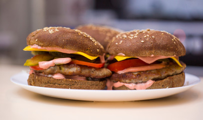 Classic hamburgers with bacon, meat, cheese, onions, tomatoes and cheese and a whole bun. On the plate. Close-up