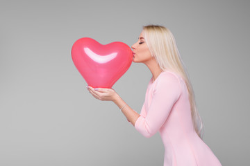Fototapeta na wymiar Beautiful young blond woman with pink heart shape air balloon on grey background. Woman on Valentine's Day. Symbol of love - Image. Space for text