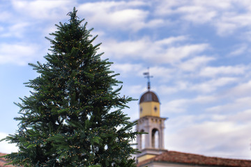 Fototapeta na wymiar Christmas tree with bell tower in background. Udine city, Friuli Venezia Giulia region, Italy.