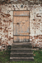 Fototapeta na wymiar Old wooden closed door and steps in ancient brick building wall