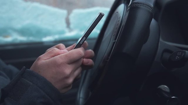 Texting in parked car while the snow is falling outside, close up of hands typing message on mobile phone, slow motion