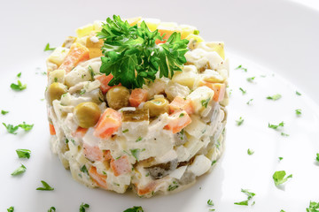 russian salad with chicken, potato, onion, carrot, pea, egg, pickled cucumber, and apple dressed with mayonnaise and decorated with parsley
