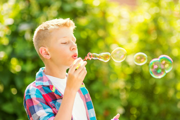 Portrait of a young boy blowing soap bubbles in a park