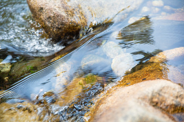 close up detail of beautiful brilliant and transparent water flowing on rocks and stones in river