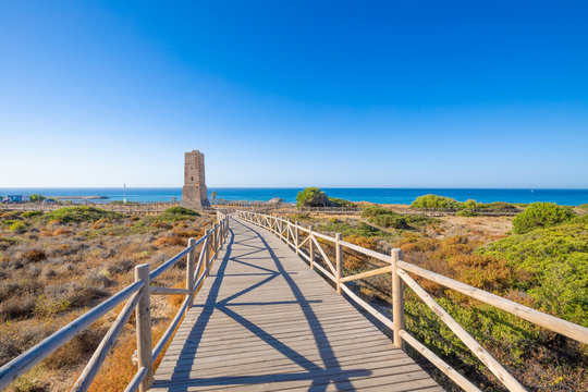 wooden footpath to ancient Thieves Tower, from year 1500, in Artola Dunes Natural Park, next to Mediterranean Sea, in Cabopino of Marbella town (Malaga, Andalusia, Spain, Europe)