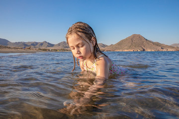 Fototapeta premium little girl sitting on the shore playing in the water of Genoveses Beach, in Cabo de Gata Natural Park (Almeria, Andalusia, Spain)