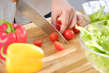 Girl cuts fresh tomatoes for a delicious salad. A variety of fresh vegetables on a wooden table.
