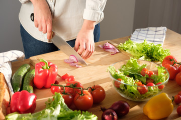 Girl cuts red onions for vegetable salad. Cooking salad