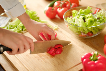 Girl cuts sweet pepper in vegetable salad. Cooking salad.