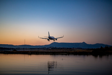 Fototapeta na wymiar Passenger airplane is landing at Corfu airport at sunset, the golden hour, airport lights are on. Kerkyra Island, Greece, clear sky spring evening
