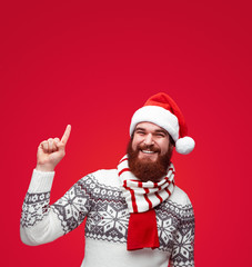 man with with santa hat pointing up to copy space over red color background.