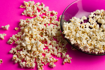 Fried popcorn scattered from glass plate on pink background. Сoncept of leisure