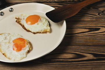 Two fried eggs in metal beige pan and dirty spatula on old wooden brown table. Copy space