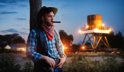 Brutal cowboy smokes a cigar on sunset
