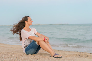 Fototapeta na wymiar Beautiful girl sitting on the beach. Middle aged woman resting at beach near the sea. young, beautiful woman with long flowing hair on the beach