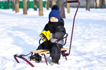 Cute little boy sitting in sleigh in winter park all around the snow