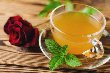 Glass cup with green tea and mint near red rose on sprig on old wooden table. Saint Valentine's Day concept