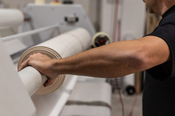 Operating a big printing machine and laminator, armed with red rolls and vinyl transparent film. Industrial worker, technical staff.