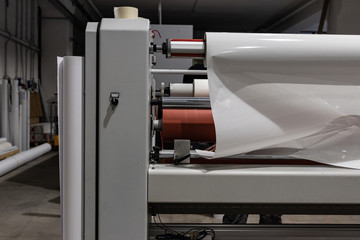 Operating a big printing machine and laminator, armed with red rolls and vinyl transparent film. Industrial worker, technical staff.