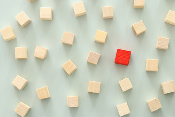 One different red cube block among wooden blocks. Individuality, leadership and uniqueness concept.
