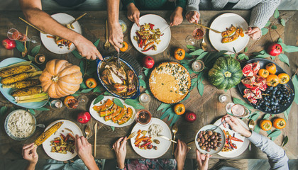 Thanksgiving or Friendsgiving holiday celebration party. Flat-lay of friends feasting at...