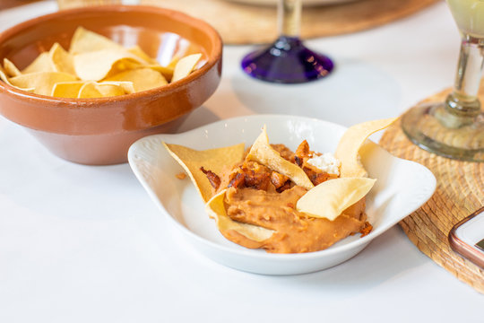Mashed Mexican beans puree in white tray with tortilla chips on restaurant table. Appetizer to share