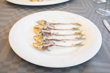 white dish with fishbone of a group of sardines cooked and eaten in a row on table of restaurant