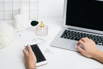 Fototapeta na wymiar Blank screen phone in women's hand and laptop keyboard on white office table