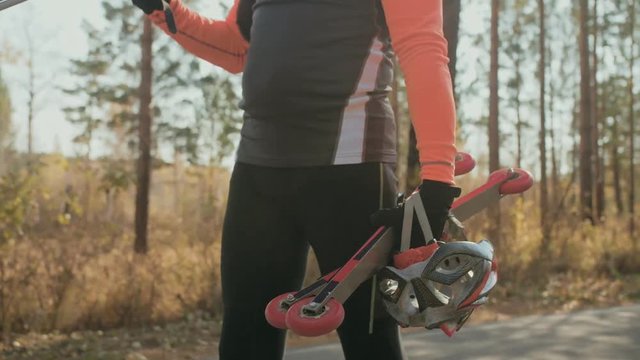 Training an athlete on the roller skaters. Biathlon ride on the roller skis with ski poles, in the helmet. Autumn workout. Roller sport. Adult man riding on skates. The athlete goes and holds sports