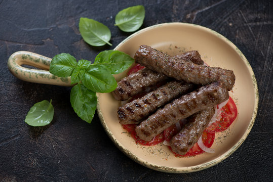Serving pan with grilled balkan cevapi or skinless beef sausages, studio shot on a dark brown stone background