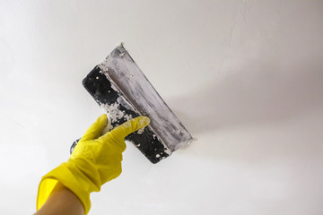 worker's hand in yellow gloves holding putty knife patching a hole with spatula with plaster or...
