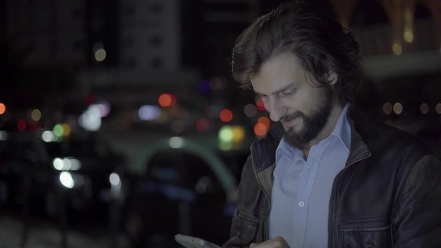 Cheerful man using smartphone in night city. Caucasian smiling freelancer working on smartphone in evening city with empty space. Remote work concept