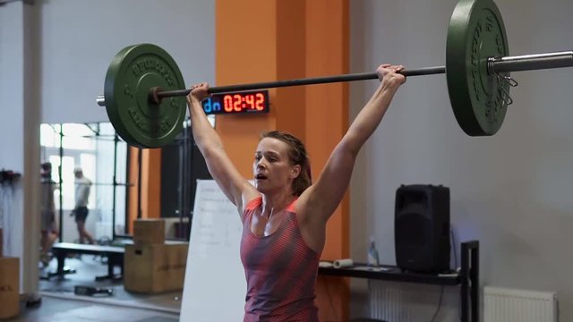 Strong woman doing weightlifting workout during cross fitness training in gym