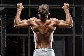 Muscular man doing pull up on horizontal bar in gym, working out. Strong fitness male pulling up,...