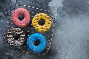 Obraz na płótnie Canvas Metal cooling rack with four different donuts, flatlay on a grey concrete background with space