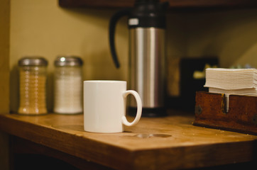 The single coffee mug on the edge of the cream and sugar station in the cafe. 