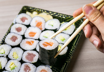Hand using chopsticks pick Sushi and Sashimi rolls on a black stone slatter. Fresh made Sushi set with salmon, prawns, wasabi and ginger. Traditional Japanese cuisine