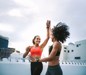 Cheerful fitness women giving high five while jogging on rooftop