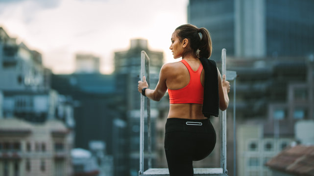 Rear view of a fitness woman standing on rooftop staircase