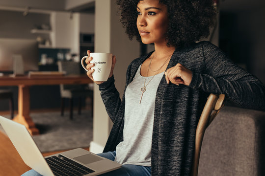 Thoughtful female having coffee while working on laptop at home