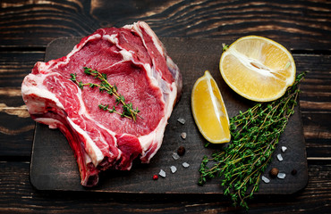 Raw steak, lemon, red pepper, garlic and seasonings on a dark rustic background