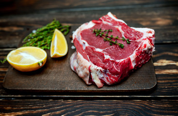 Raw steak, lemon, red pepper, garlic and seasonings on a dark rustic background